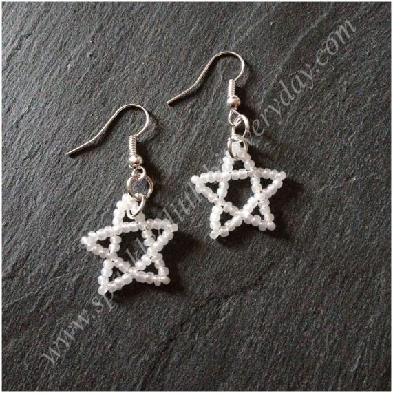 Star earrings made from tiny white beads lying on a slab of grey slate.