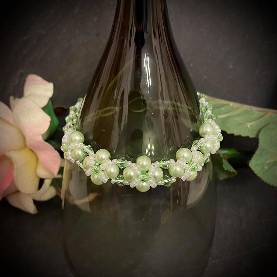 Alicia bracelet made from green pearls and crystals displayed on a wine glass.