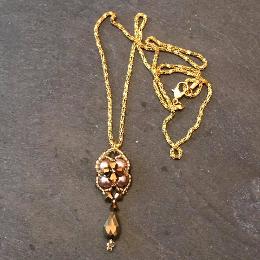 Lady Victoria pendant on a gold chain, lyin on a grey slate.