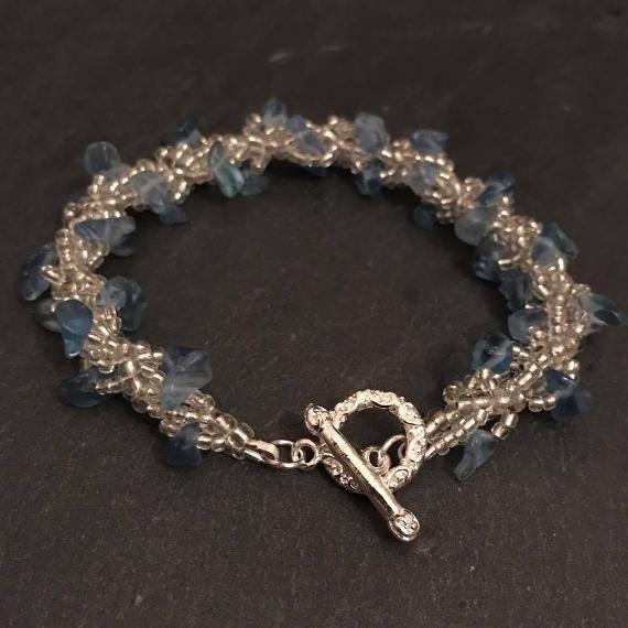 Spiral rope bracelet made with silver beads and blue glass chips, fastening with a silver toggle clasp.