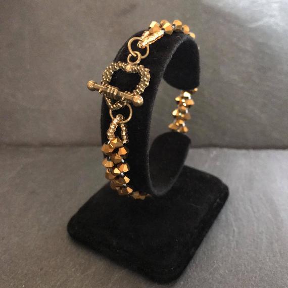 Right angle weave bracelet made from gold crystal bicones on a black velvet bracelet stand.