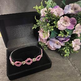 Pink bracelet in a black velvet box with purple flowers.