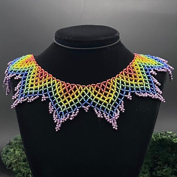 A lace collar necklace made from black, grey, silver, and white beads in front of a silver tinsel background..