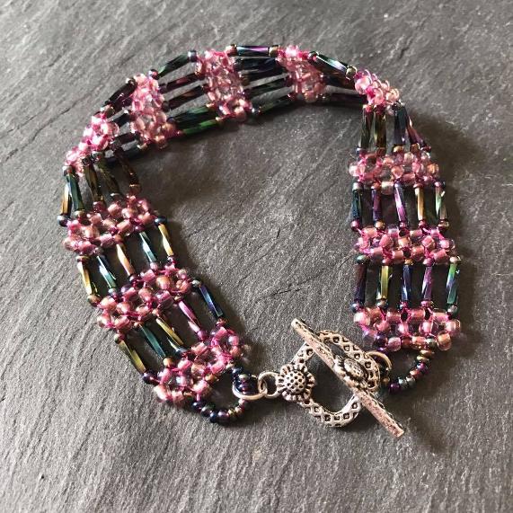 Steel Gate bracelet made from purple beads with a ready made sunflower-patterned toggle clasp, lying on a grey slate board.