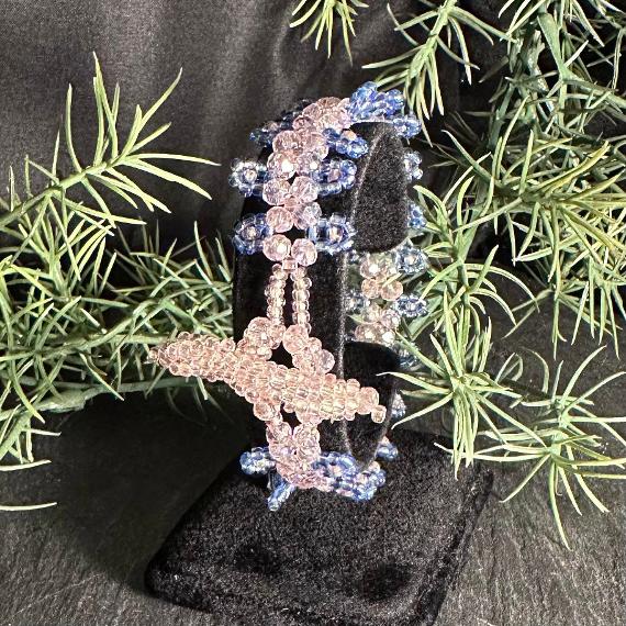A pink and blue bracelet on a velvet stand with leaves in the background.