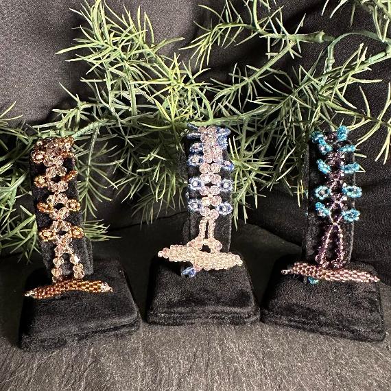 Three crystal and seed bead bracelets on velvet stands with greenery in the background.
