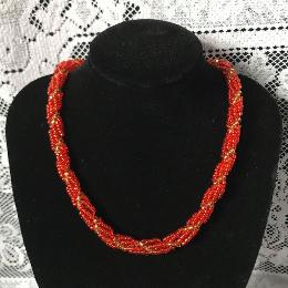 Red spiral rope necklace on a blacj velvet bust in front of a white lace cloth.