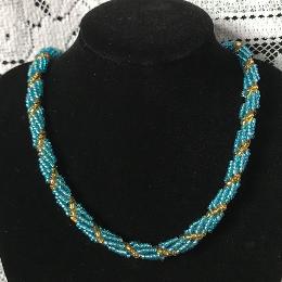 Turquoise and green spiral rope necklace on a black velvet dispaly bust in front of a white lace cloth.
