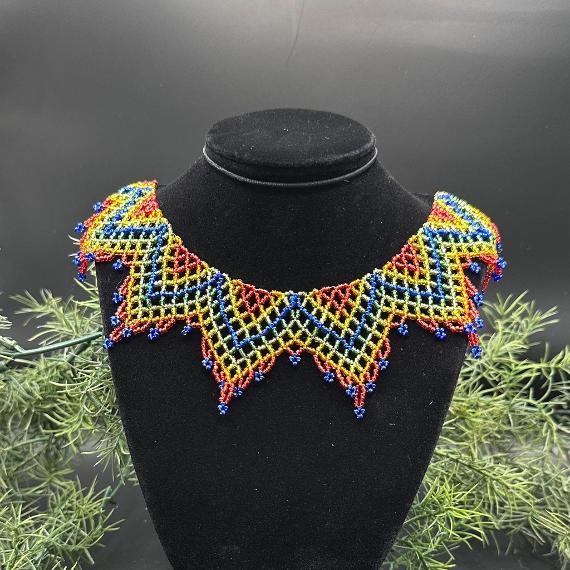 A lace collar necklace made from black, grey, silver, and white beads in front of a silver tinsel background..